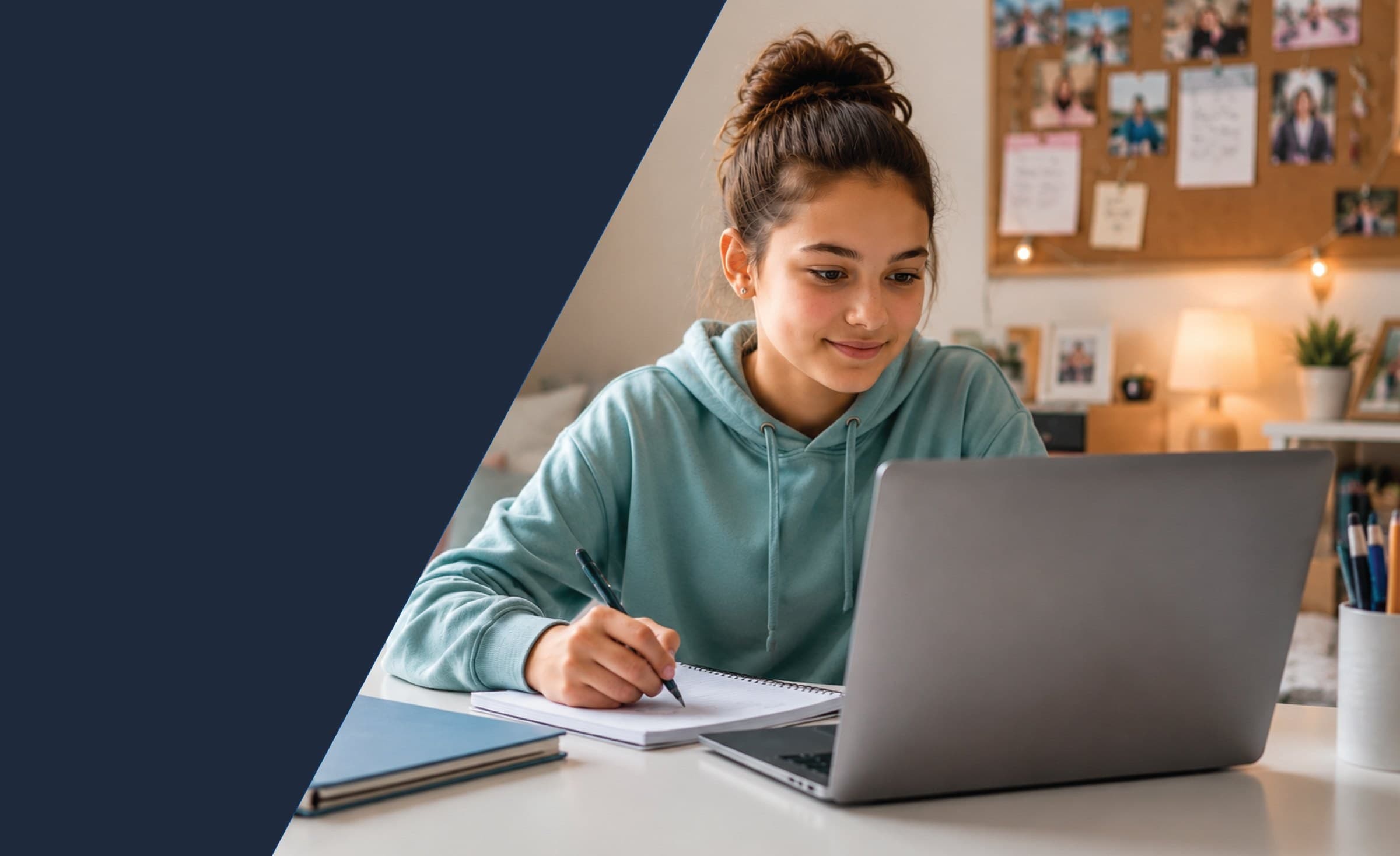 A student working at a laptop in her bedroom, writing in a notebook beside it.